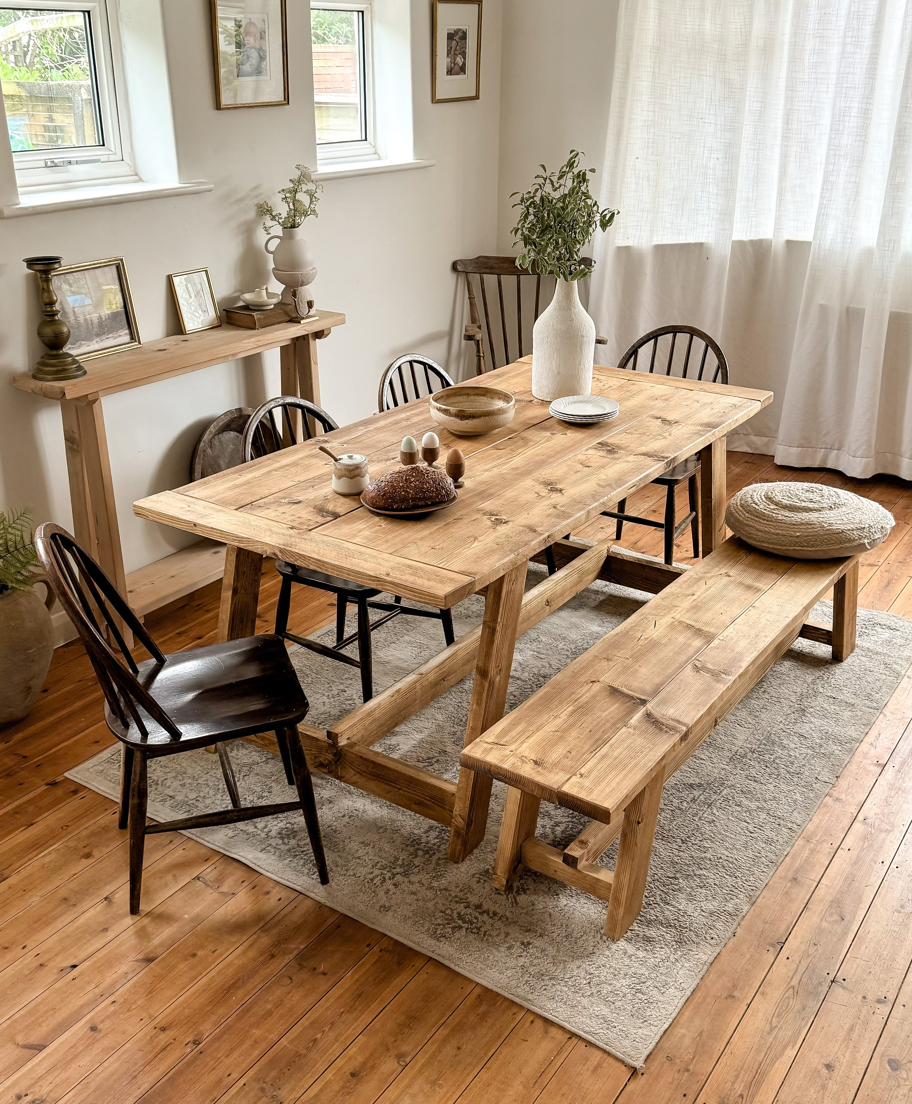 Dining table with bench and 4 chairs, in antique oak with decor items on a light coloured rug. The dining table is solid wood, made from reclaimed wood and is rustic.