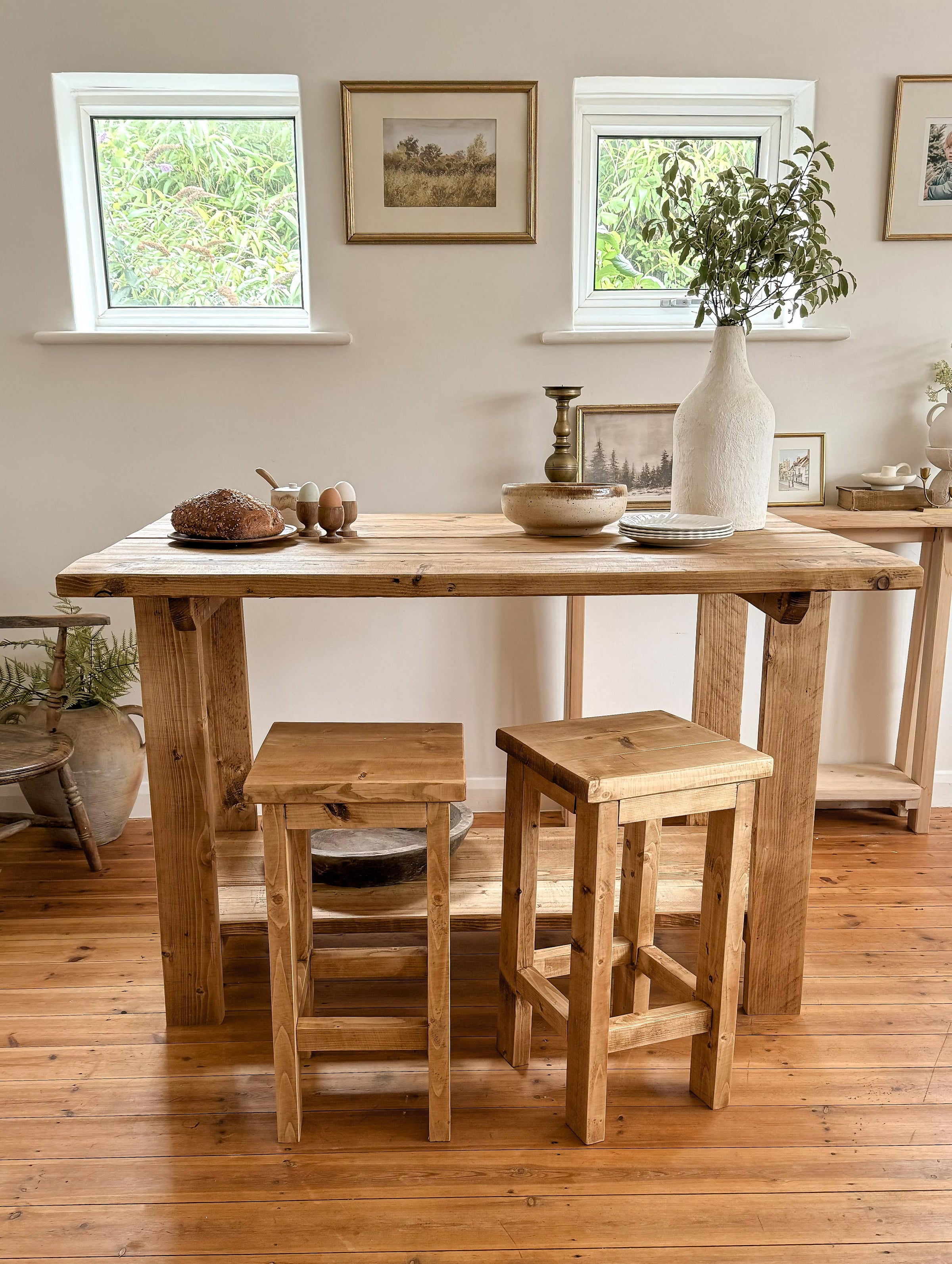 Breakfast bar table with flowers and a white wall, 2 stools and a wooden floor.