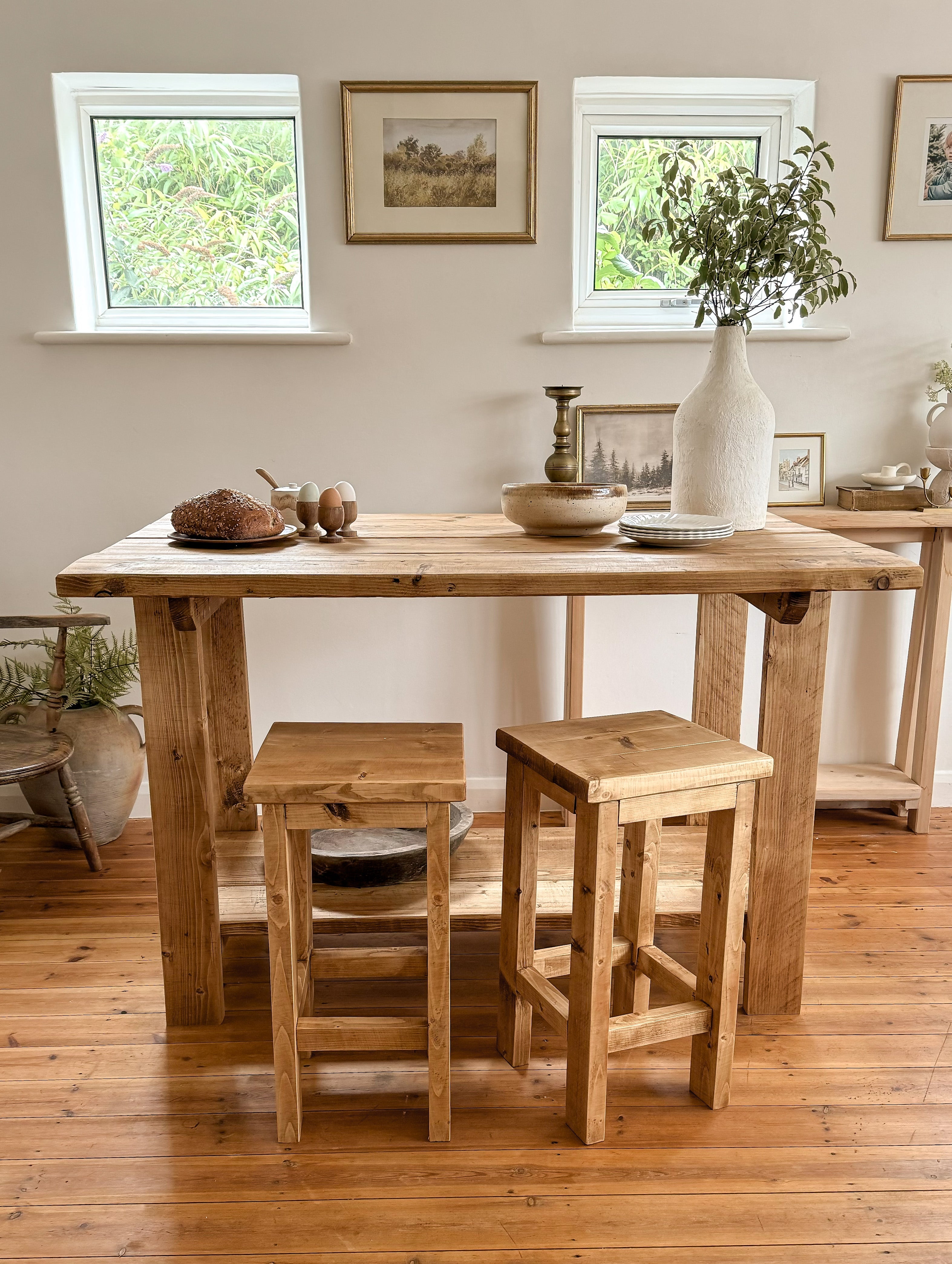 Breakfast bar table with flowers and a white wall, 2 stools and a wooden floor.