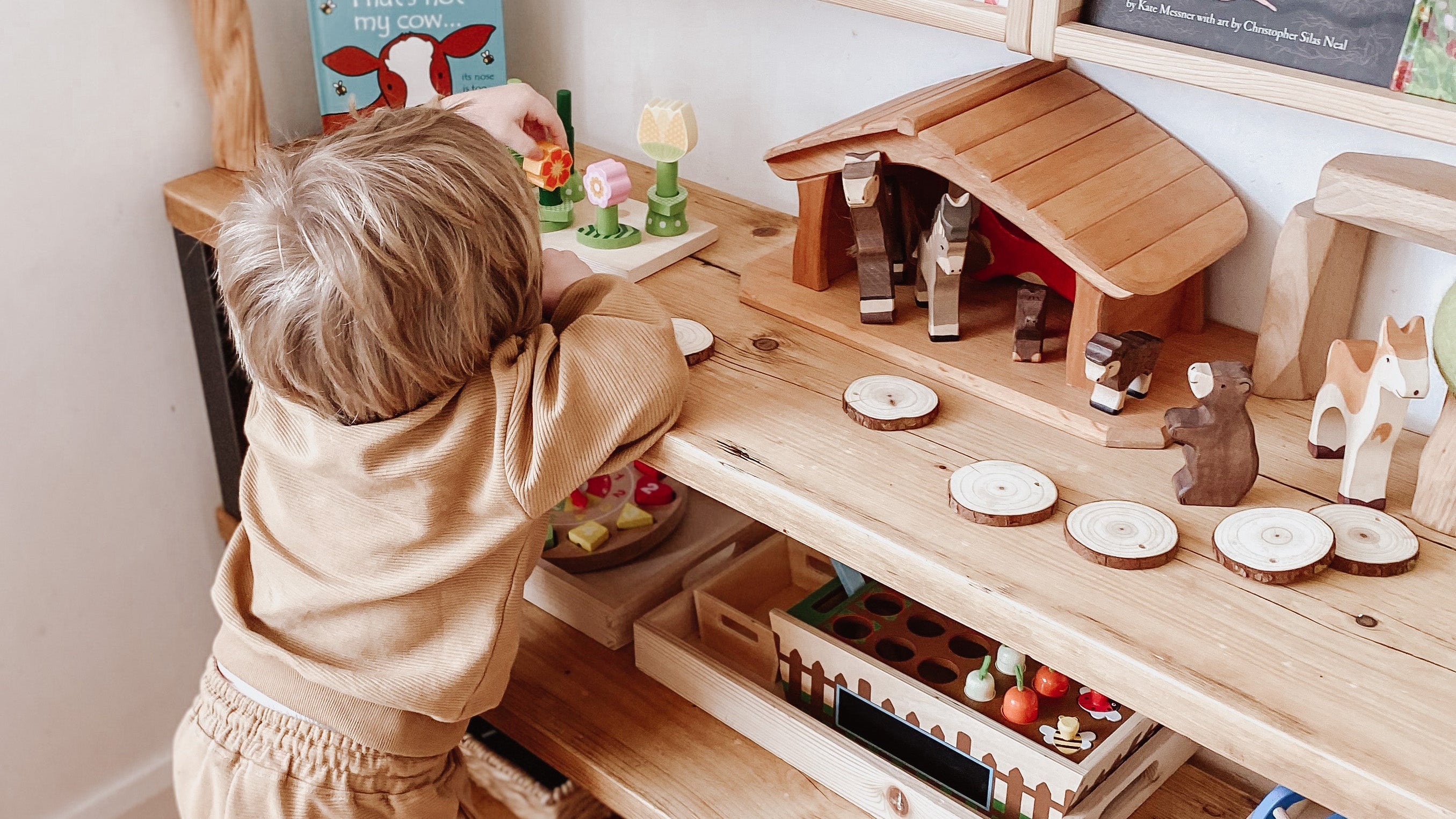 Child playing with a wooden toy kitchen set in a room with books on a shelf.