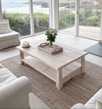 Whitewashed coffee table in a Modern living room with large windows, white furniture, and a fireplace.