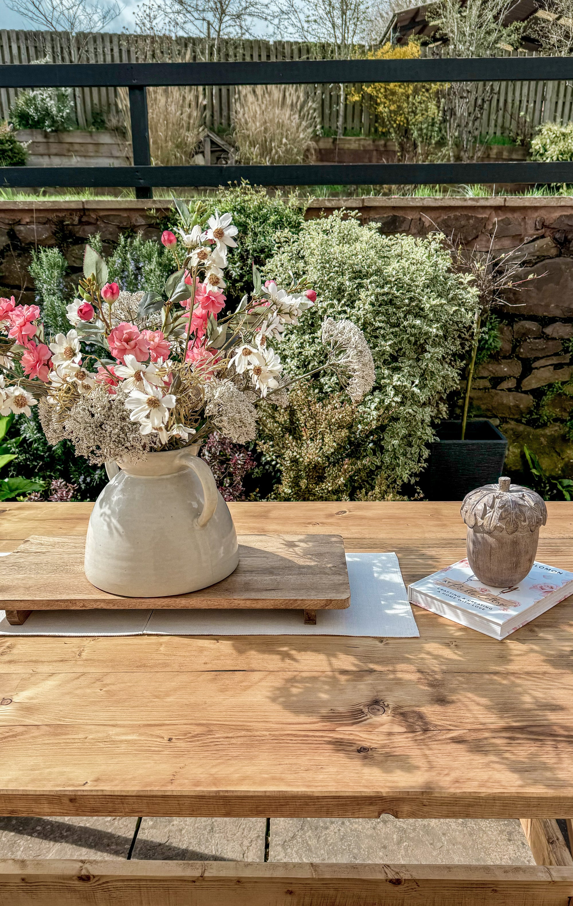 Floral arrangement in a white vase on a wooden table with a garden background
