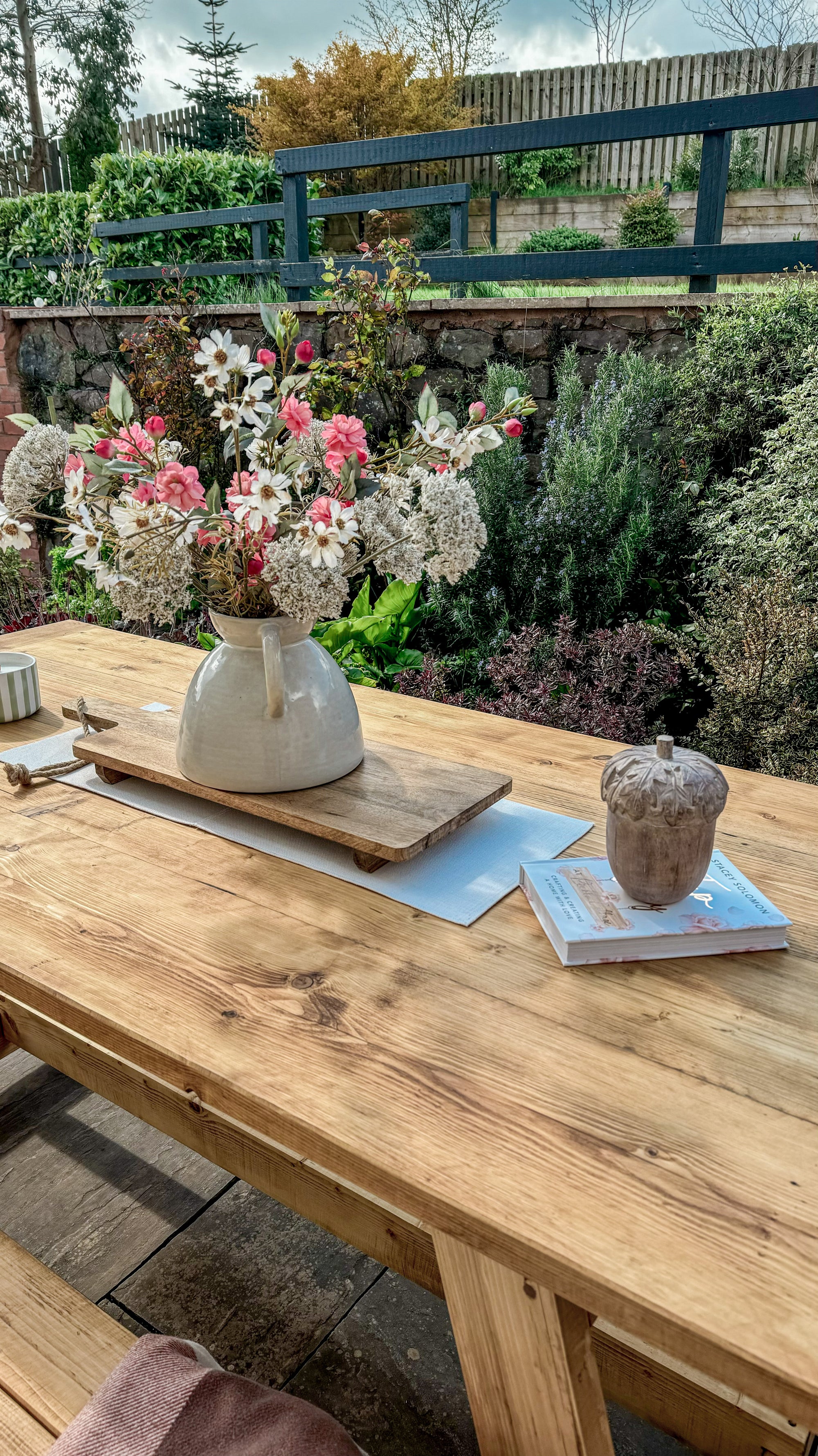 Floral arrangement in a vase on a wooden table with a garden background