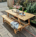 Wooden outdoor table with benches and a vase of flowers in a garden setting.