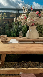 Wooden table with decorative items including a vase of flowers and a teapot in an outdoor setting.