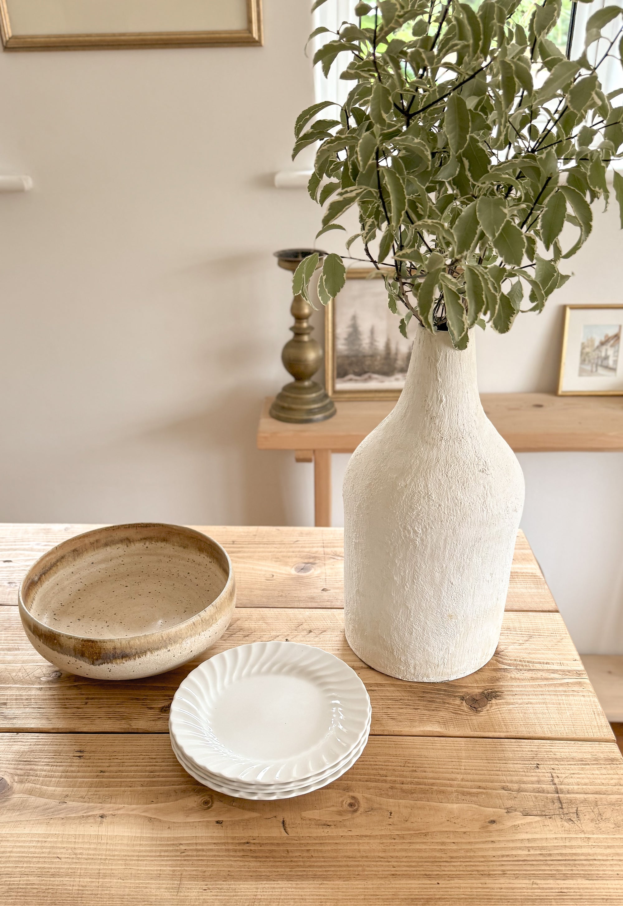 Decorative items including a vase, plates, and a bowl on a wooden bar table with a neutral background.