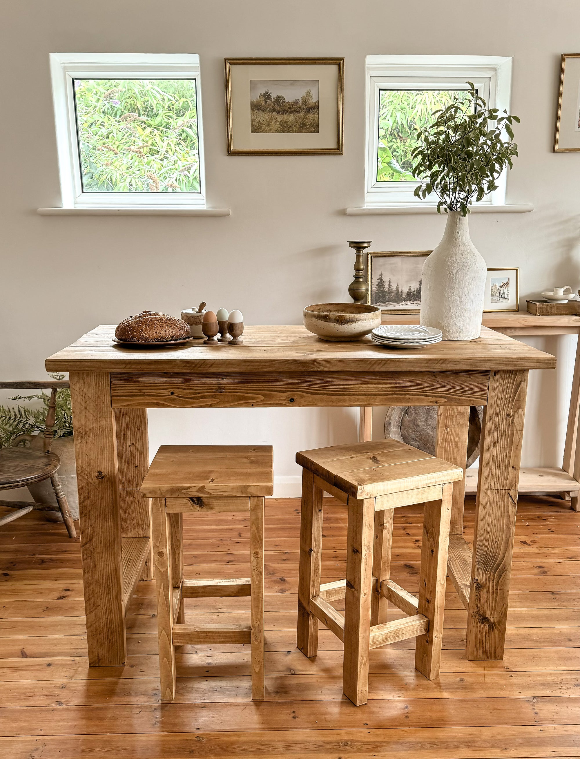 Bar table with stools in a room with windows and framed pictures.