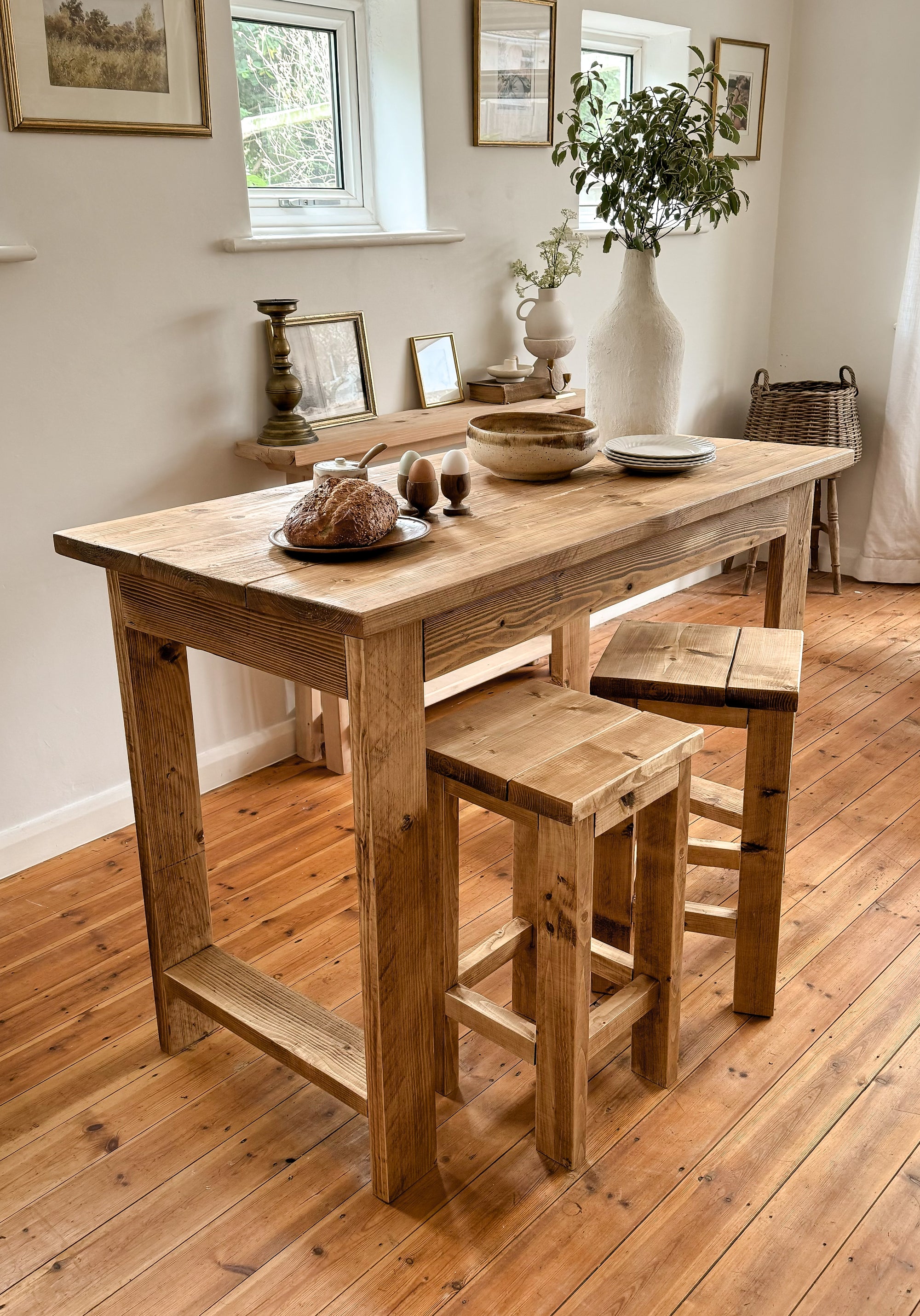 Wooden bar table with stools in a room with wooden flooring and framed pictures on the wall.