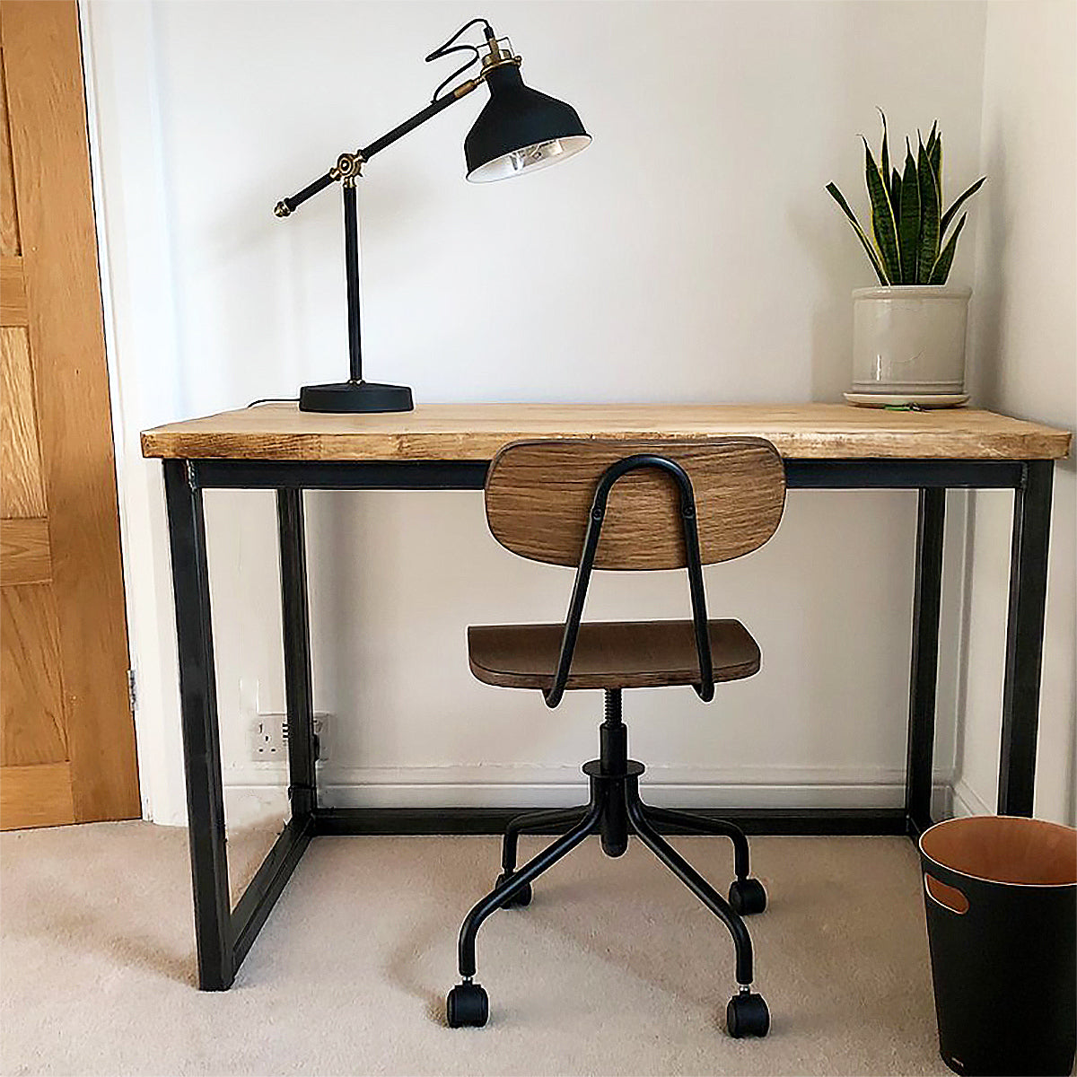 wooden desk with a black lamp and plant and desk chair